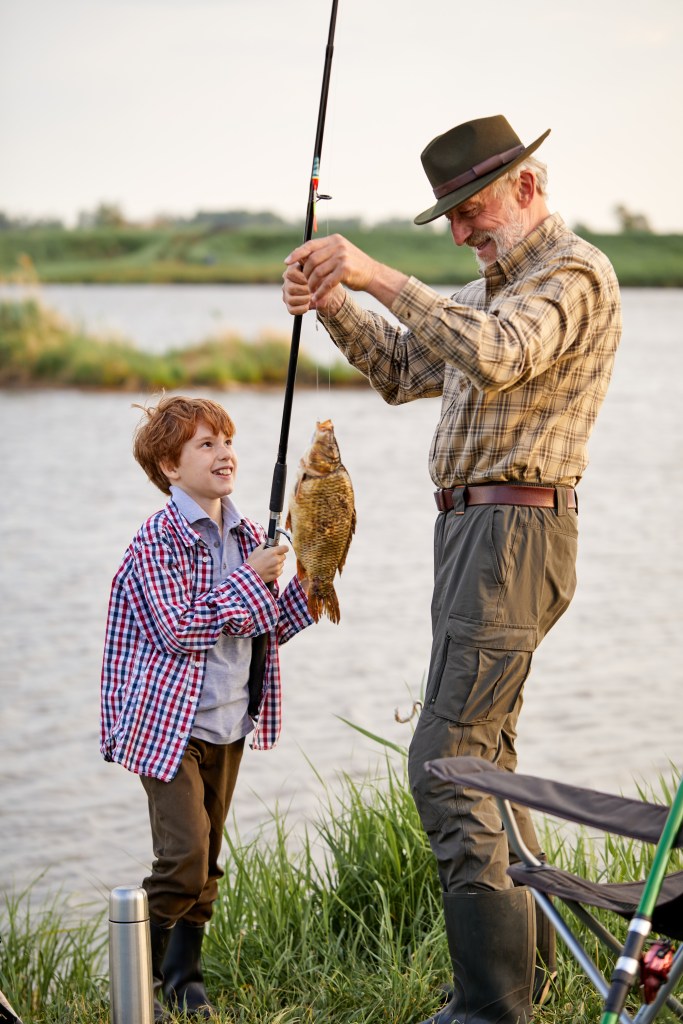 Catch of the day. Happy grandfather and child boy fishing while on the shore of pond